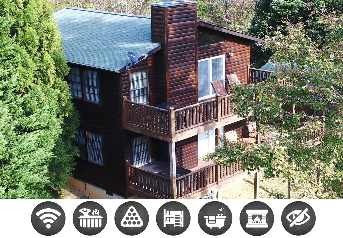 A charming wooden cabin exterior nestled among lush greenery, featuring a spacious balcony perfect for relaxing or outdoor dining. The scene captures the inviting balcony at sunset, with a rustic chimney adding character and the surrounding mountains hinting at peaceful seclusion.