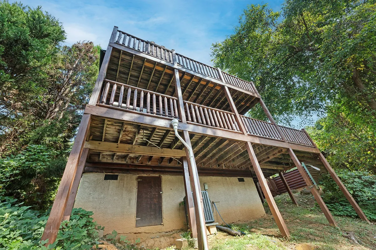 A multi-level wooden deck overlooks abundant greenery, with ample space for outdoor gatherings, relaxation, and social activities. The setting suggests flexibility for both large and intimate group moments.