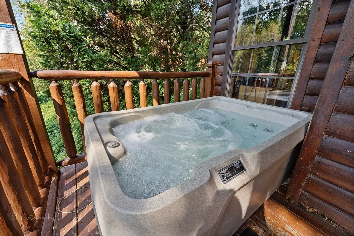 A cozy hot tub sits on a wooden deck, surrounded by green foliage and a sturdy railing. The scene suggests an inviting spot for parents to relax while children play, or for the whole family to gather and recount the day's adventures.