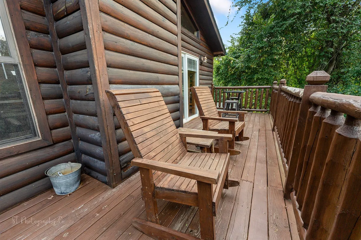 This image features classic wooden rocking chairs lined up on a deck, with a wooden railing and a lush green forest visible in the background. The inviting setup is shaded and tranquil, emphasizing a close connection to the surrounding woods and offering a spot for peaceful relaxation and appreciation of nature.