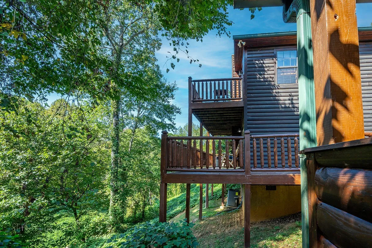 A rustic wooden balcony extending from a log cabin, nestled among mature trees. The balcony provides a cozy, intimate space for stargazing or morning coffee, with nature enveloping the retreat.