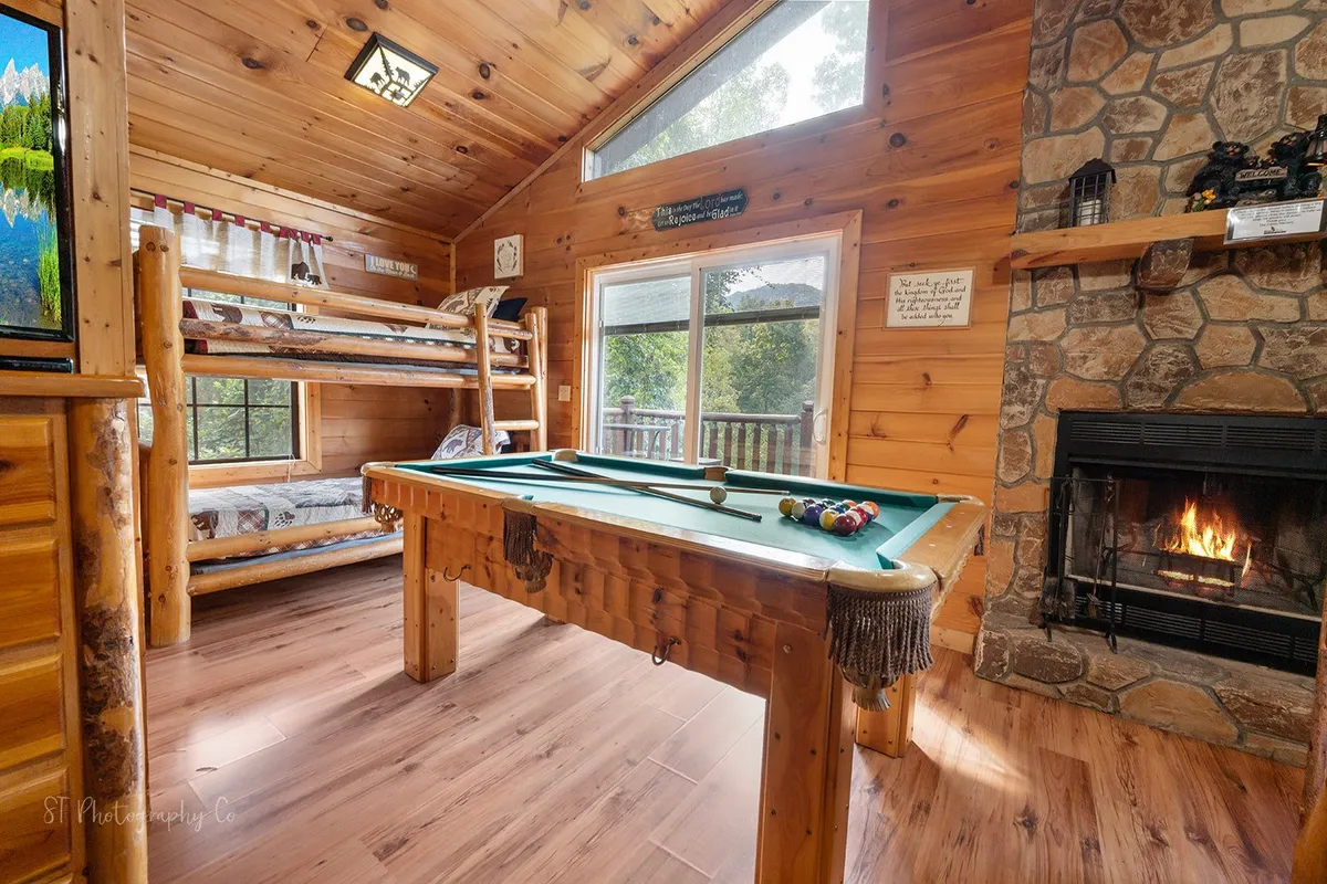 Inside, a vibrant upper-level suite features a pool table, cozy fireplace, bunk beds, and expansive windows. The arrangement is inviting for both friendly competition and shared downtime, capturing the spirit of playful group activity.