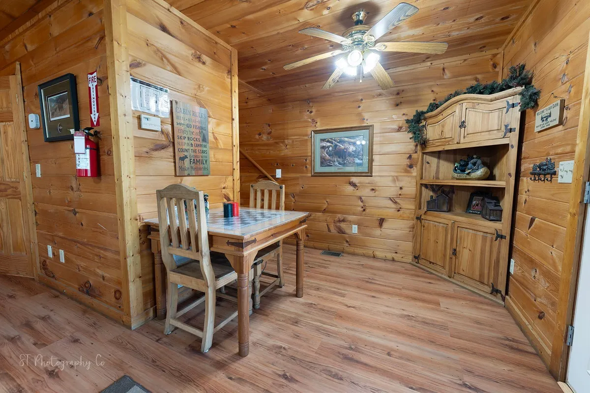 A wooden dining table surrounded by matching chairs takes center stage in this inviting space. The dining area is accented with a ceiling fan, decorative shelving, and framed artwork, creating an atmosphere suitable for family meals or group gatherings.
