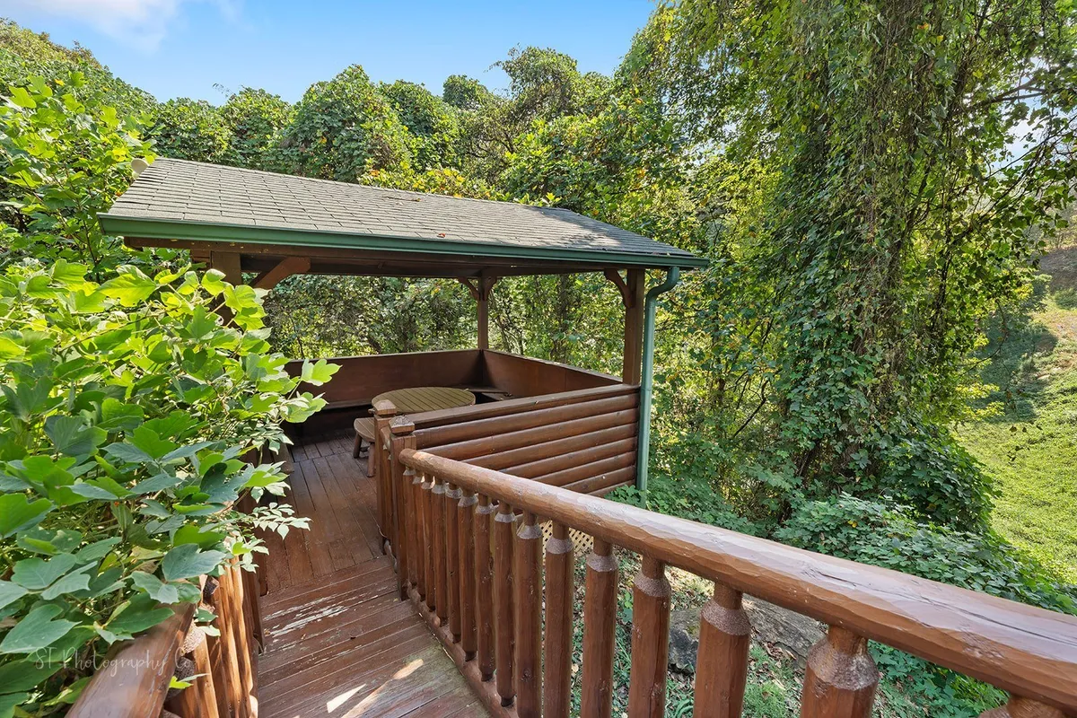 This image captures a wooden gazebo nestled among lush greenery, enclosed by a wooden railing. The tranquil setting invites guests to relax, read, or enjoy casual outdoor meals, embodying the spirit of group gatherings in nature.