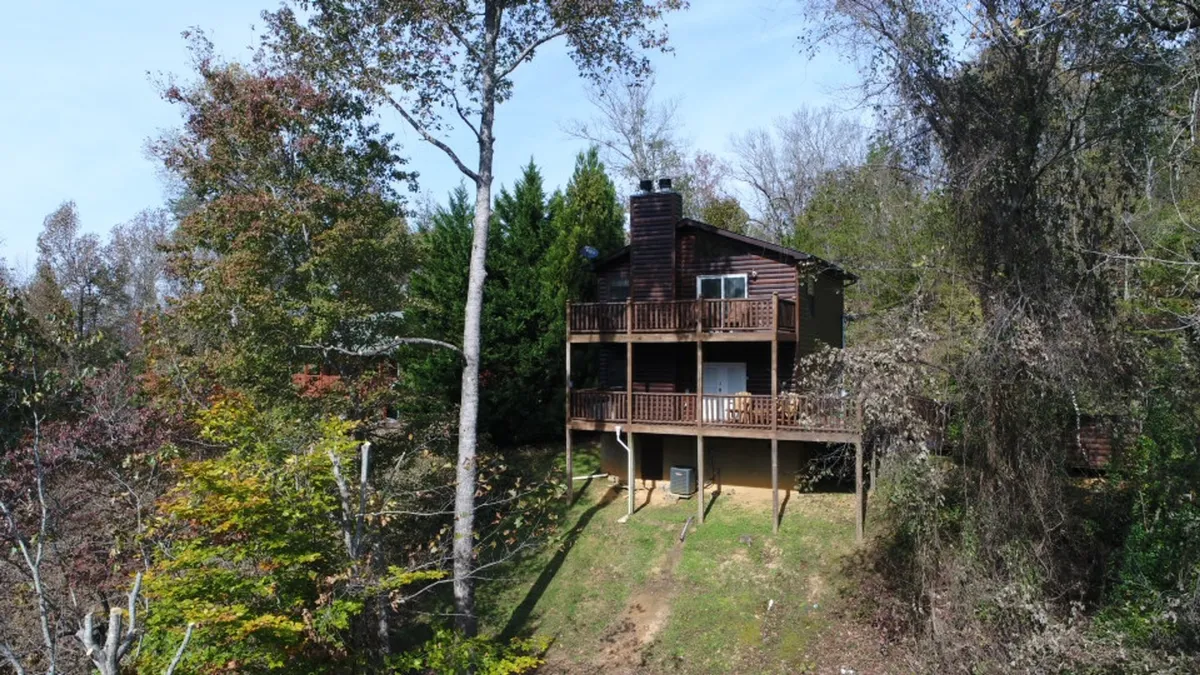 This image features a spacious wooden deck with a clear view of the surrounding tree line and part of the house's exterior. The setup suggests relaxation and enjoying the natural mountain setting, with space for family members to gather after a day of adventure.