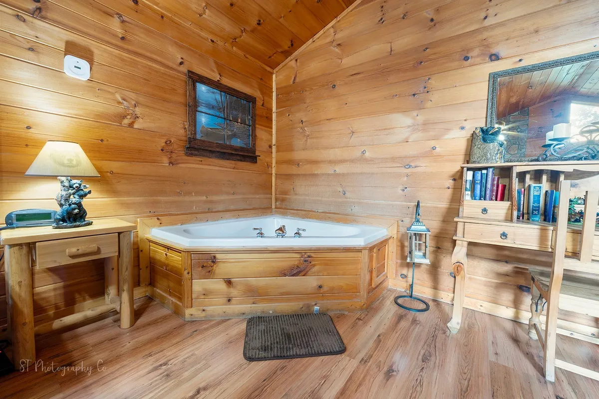 A tranquil corner of the suite with a jacuzzi tub, set beside wooden accents and a soft-lit lamp, offering a peaceful spot for unwinding after a day of fun. Books on the shelf add a touch of homely relaxation, inviting guests to soak and recharge in privacy.
