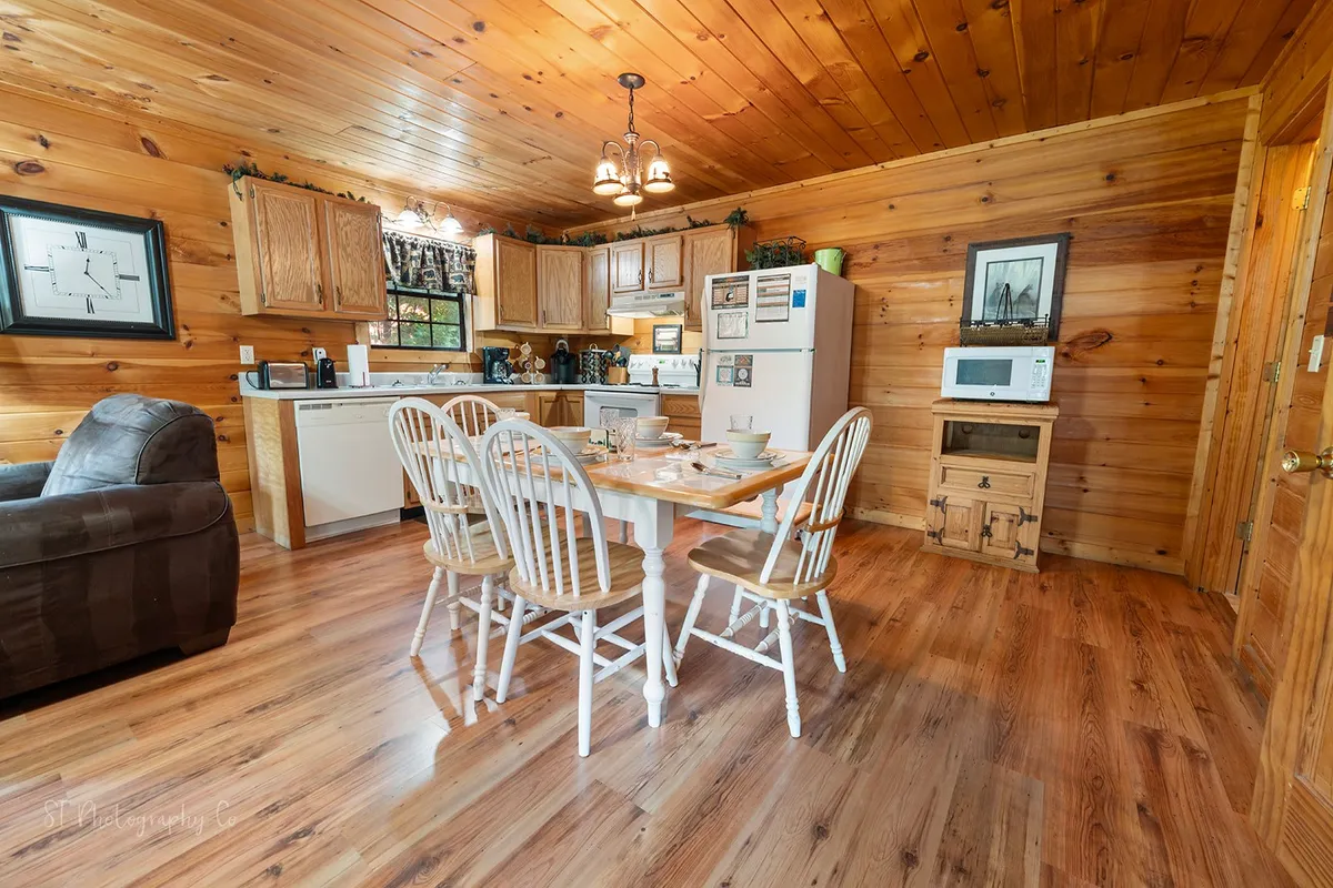 A bright, open kitchen and dining area with a wooden dining table, white chairs, modern cabinets, and stainless steel appliances. The space is laid out for family meals and group cooking, exuding a welcoming, functional atmosphere.