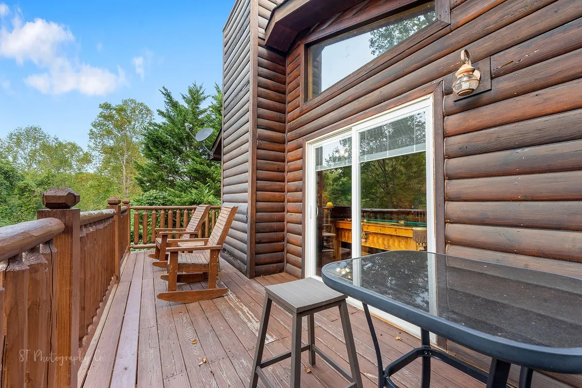 This view captures a wooden deck with Adirondack chairs arranged for conversation, glass sliding doors connecting the indoors and outdoors, and abundant greenery in the background. The area looks perfect for morning coffee, relaxing after a hike, or gathering outdoors with friends.